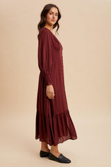 woman wearing a burgundy long sleeve maxi dress with a tiered skirt and dotted texture, standing in profile
