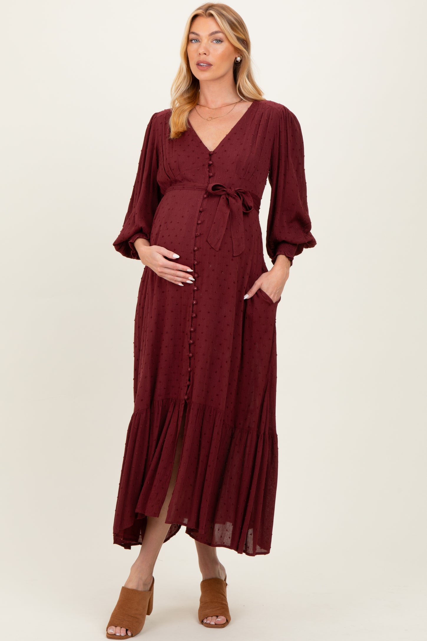 woman wearing a burgundy maternity dress with buttons, a tie waist, and long sleeves, showing a baby bump