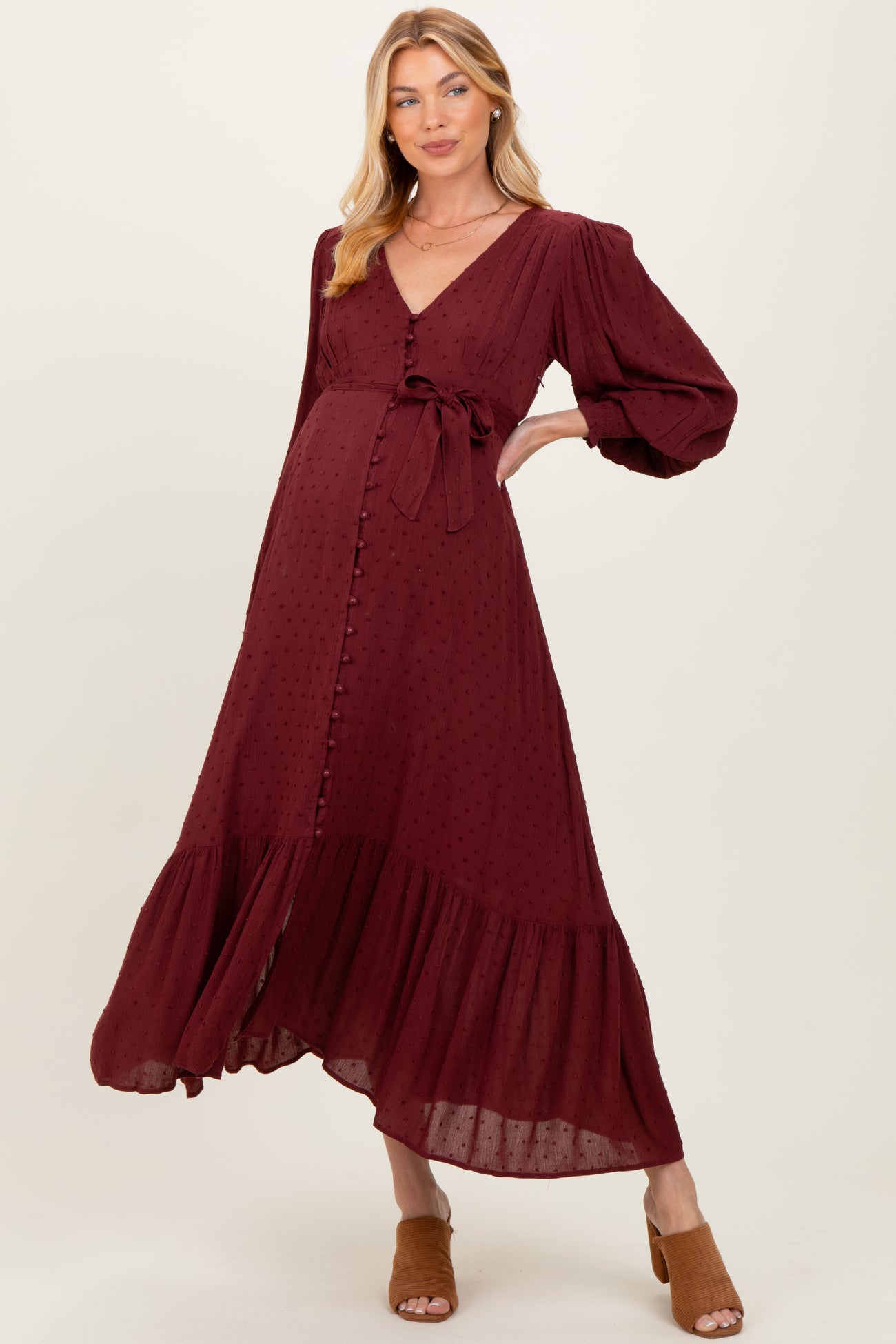 woman wearing a burgundy maternity dress with a tie waist, buttons, and puff sleeves, showcasing her baby bump