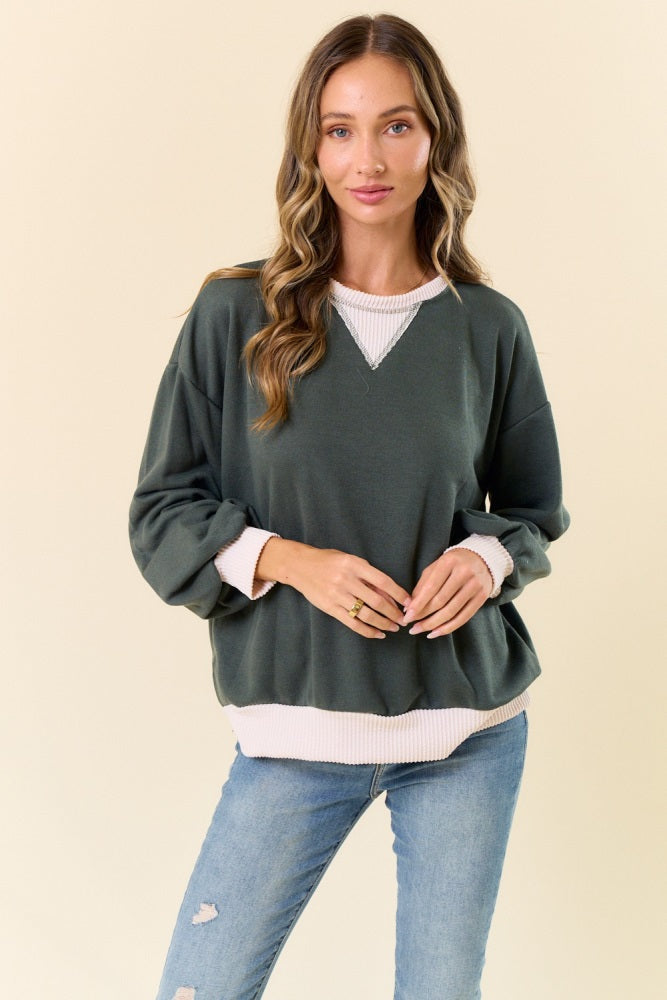 woman wearing a green oversized sweatshirt with a white ribbed hem and cuffs, paired with light blue jeans