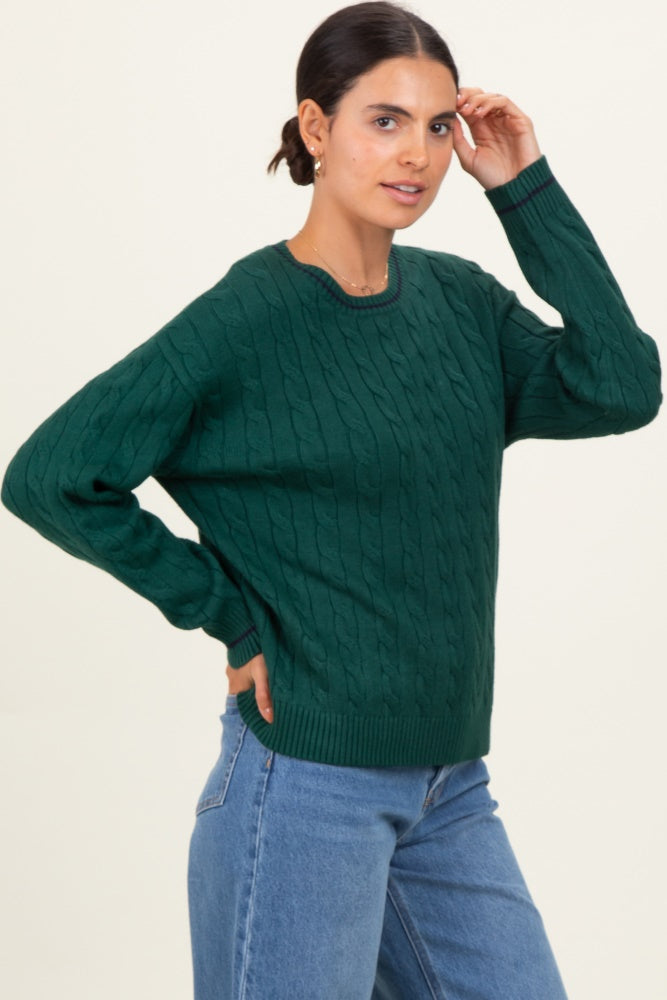 woman wearing a green cable knit sweater with a round neckline and relaxed fit, paired with blue jeans