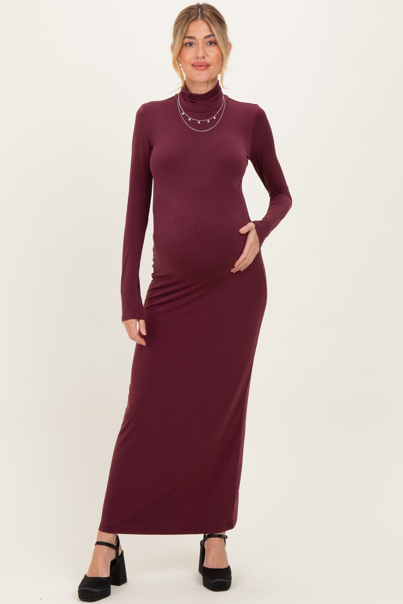 woman wearing a burgundy long sleeve maternity dress with a turtleneck and holding her baby bump