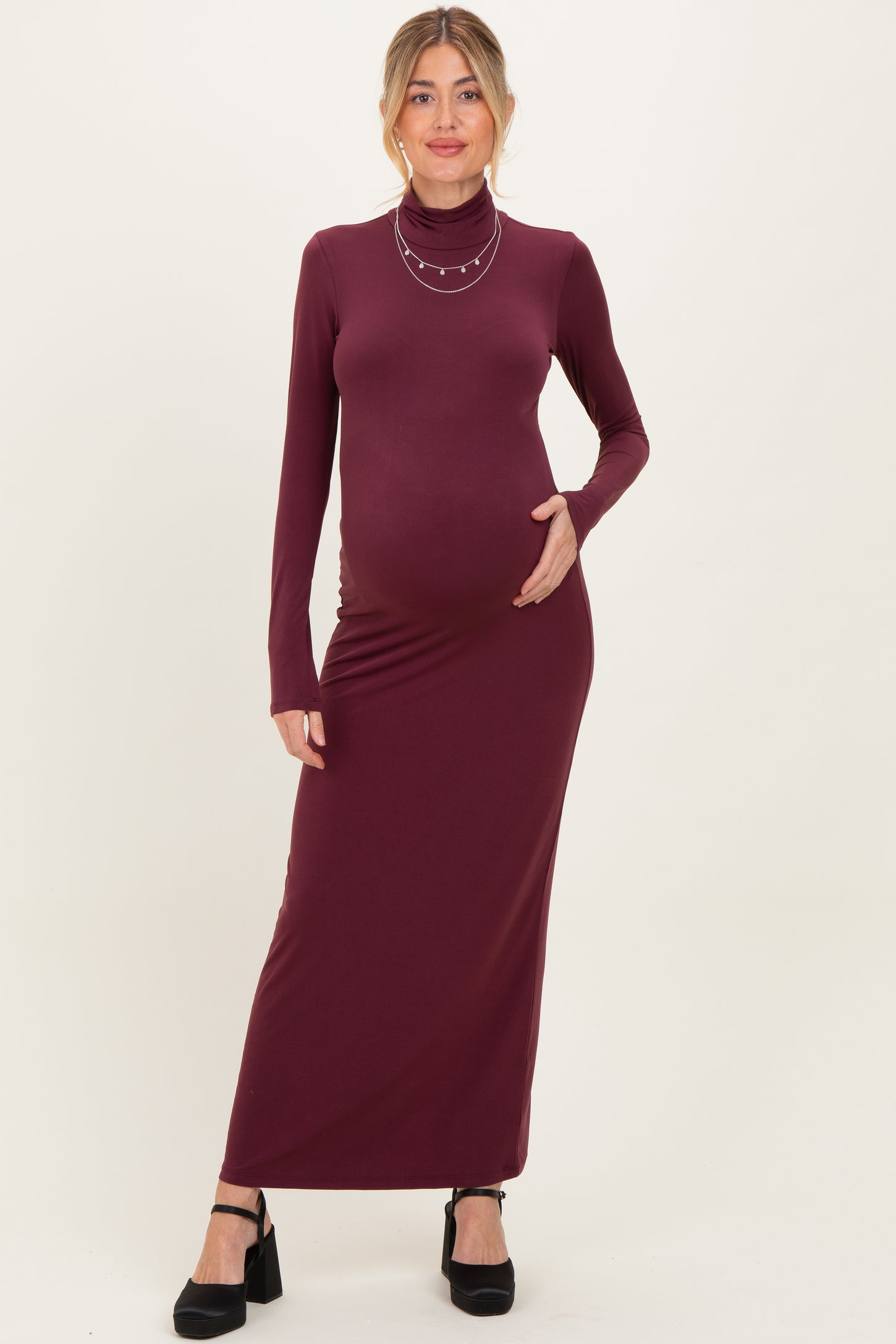 woman wearing a burgundy long sleeve maternity dress with a turtleneck and holding her baby bump