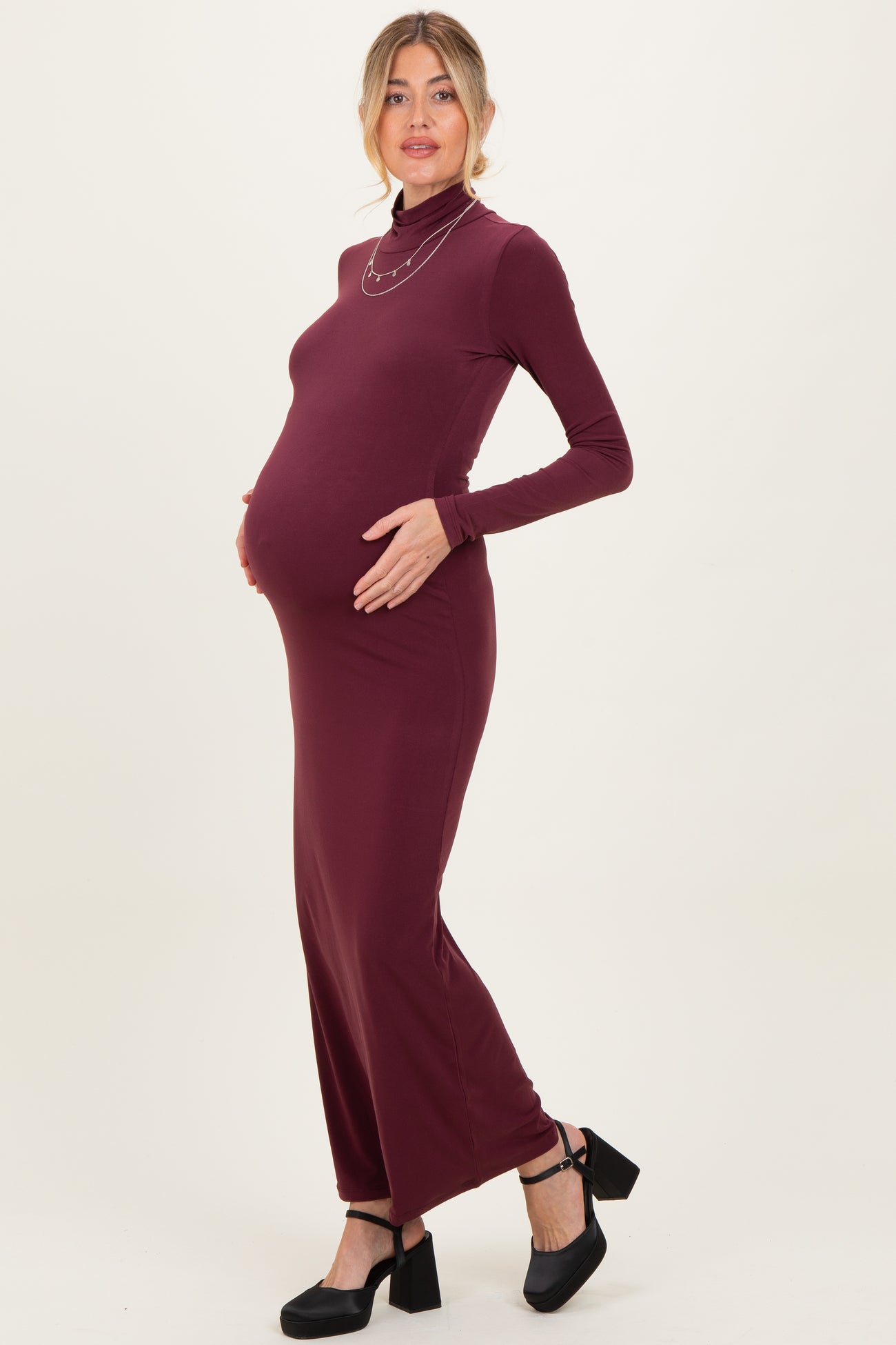 woman wearing a burgundy long sleeve maternity dress with a high neckline, showcasing her baby bump