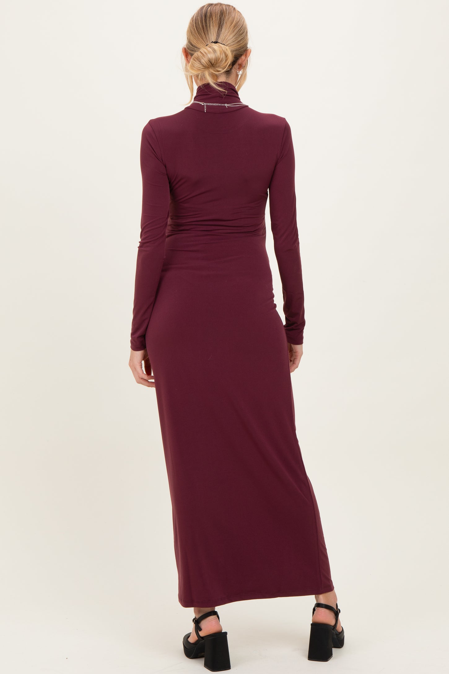 woman wearing a burgundy long sleeve maternity dress, featuring a fitted design and a maxi length from the back