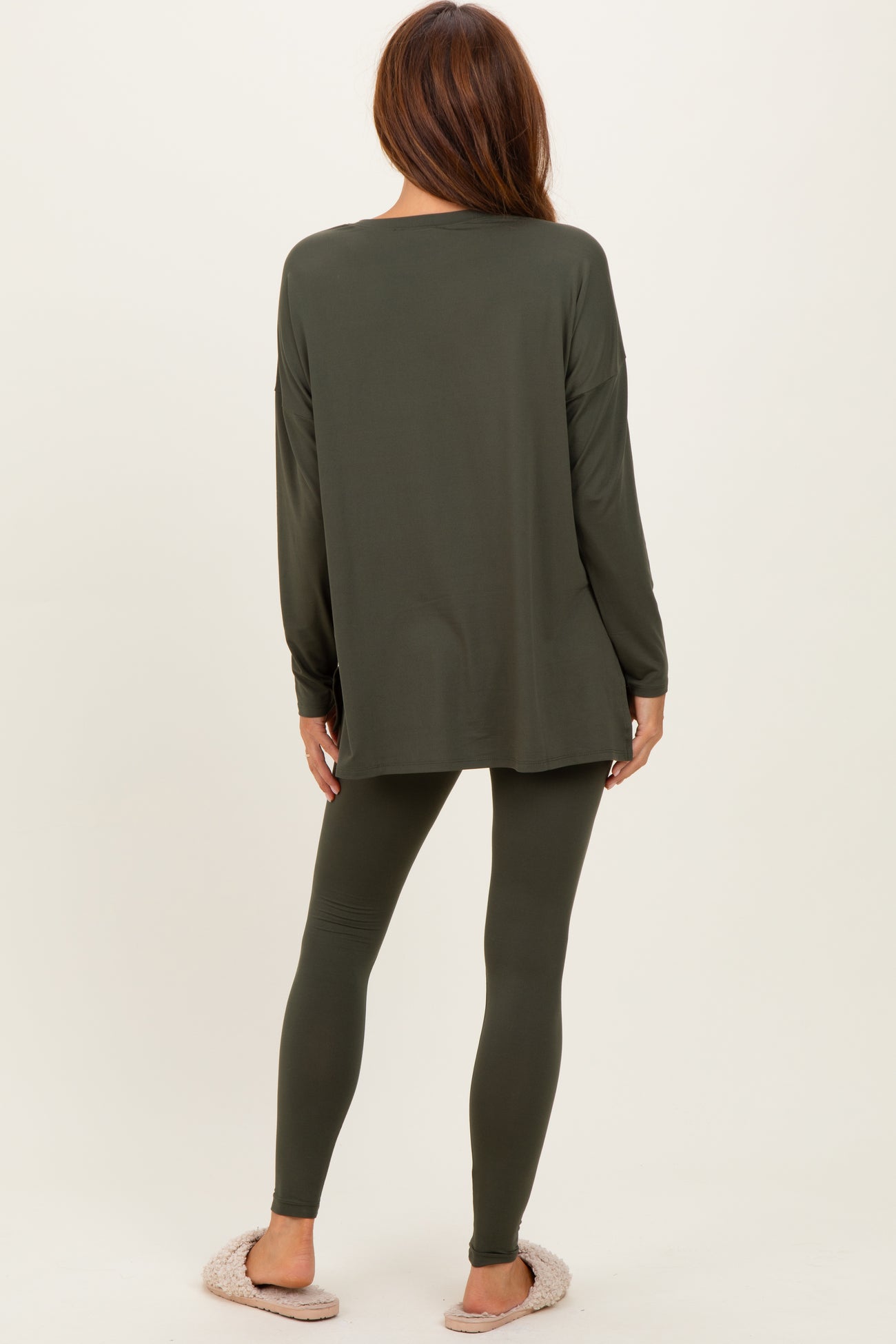woman wearing an olive green long sleeve top and matching leggings, viewed from the back, with cozy slippers