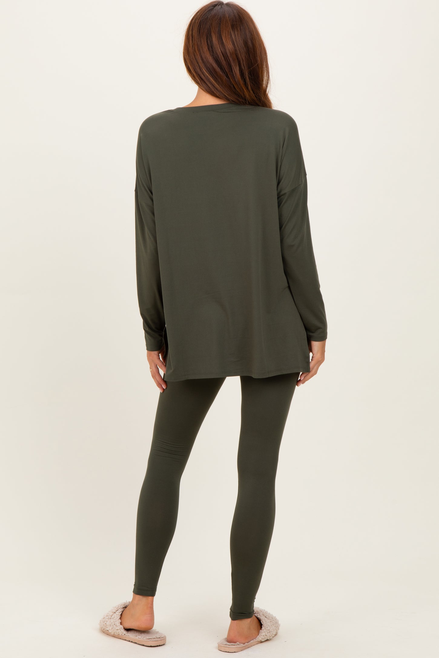 woman wearing an olive green long sleeve top and matching leggings, viewed from the back, with cozy slippers