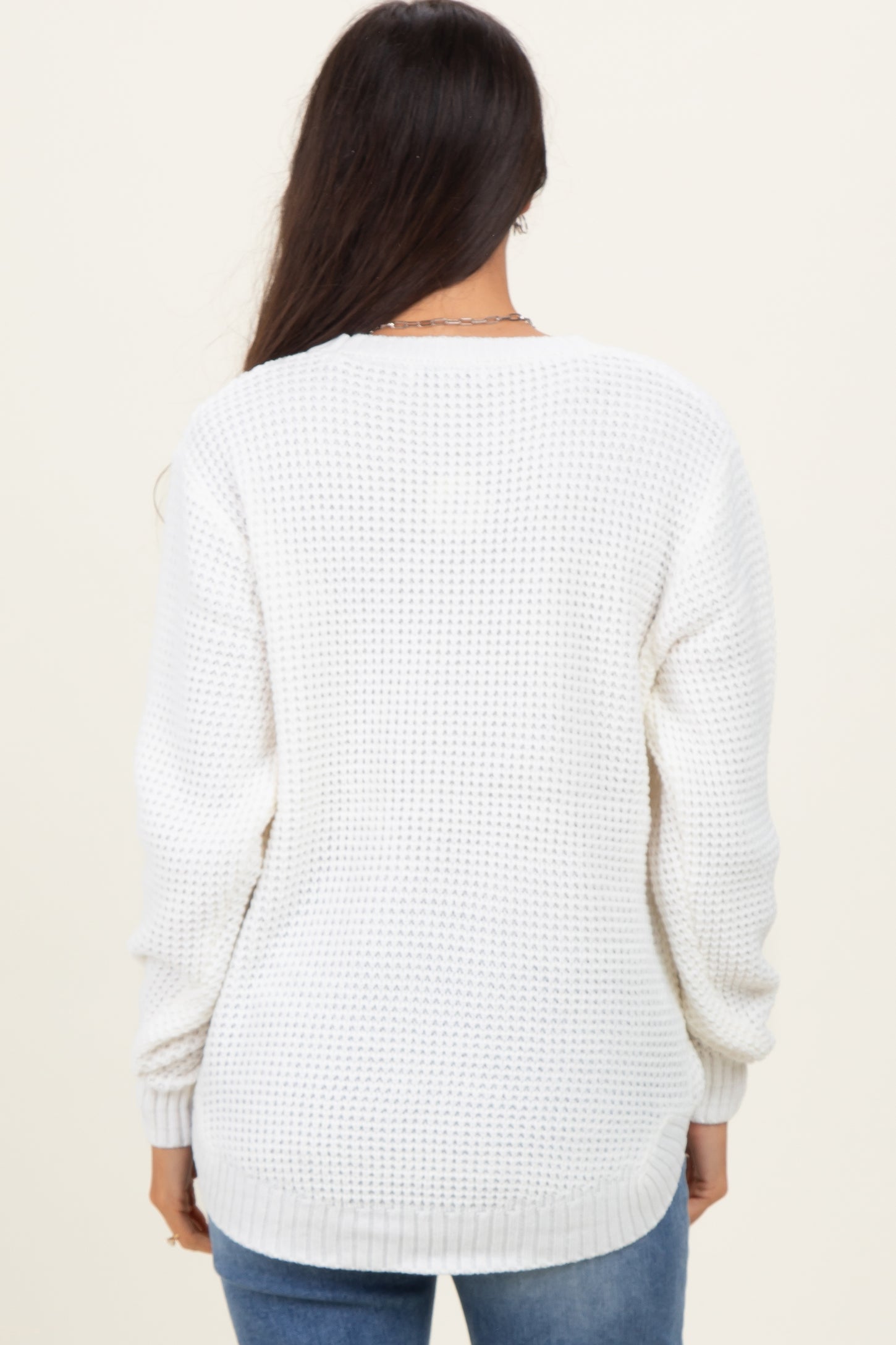 woman wearing a white waffle knit sweater with long sleeves and a relaxed fit, viewed from the back