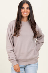 woman wearing a beige oversized sweatshirt and light blue jeans, smiling with her hand on her hip