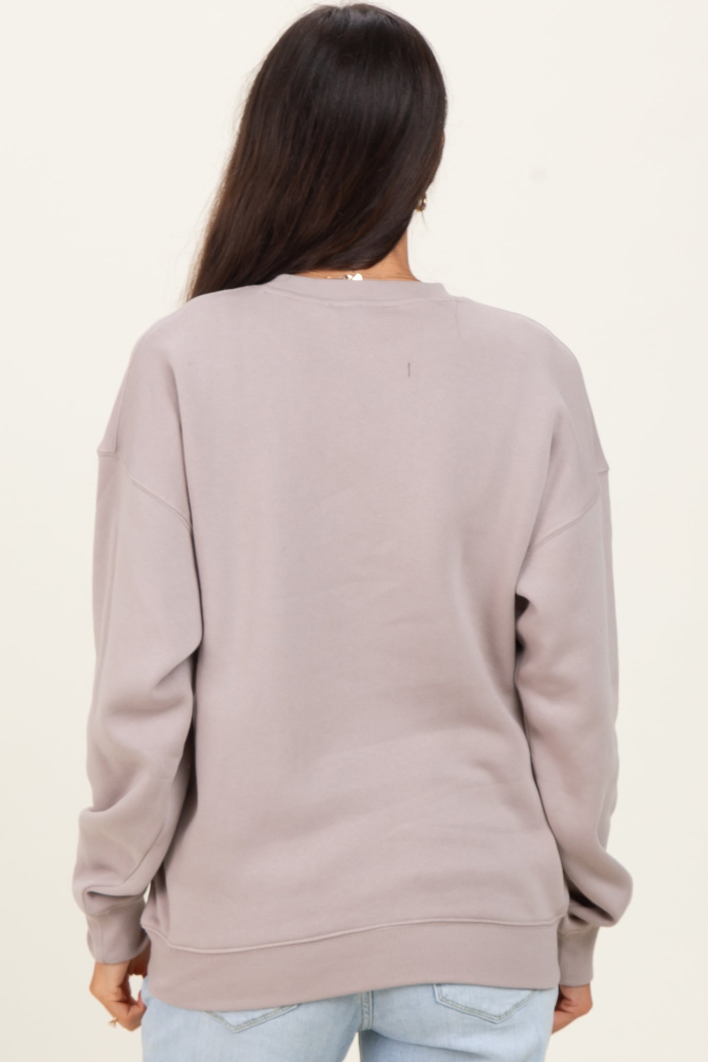 woman wearing a taupe oversized sweatshirt with dropped shoulders and a crew neck, seen from the back