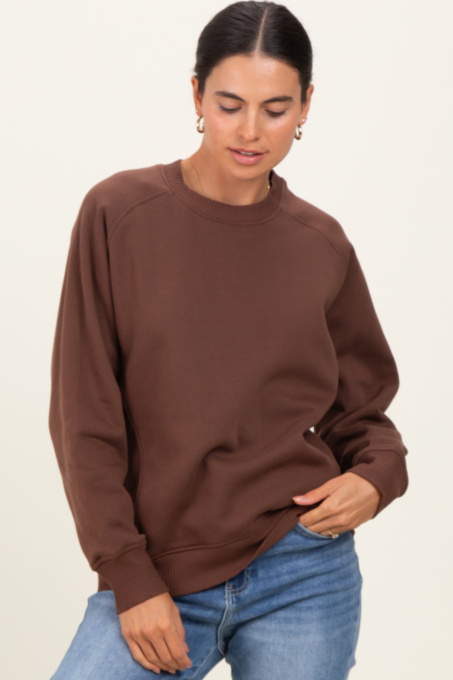 woman wearing a brown oversized sweatshirt with ribbed cuffs and a crew neckline, styled with blue jeans