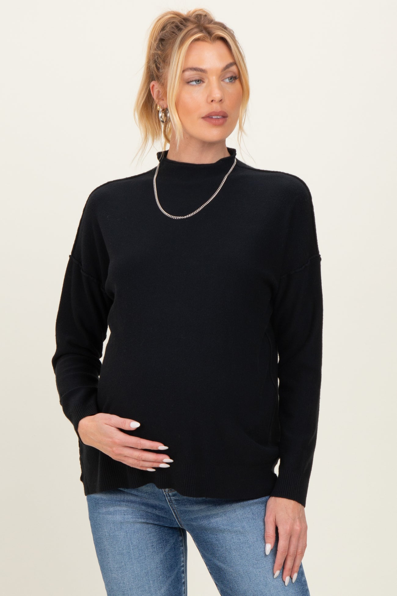 woman wearing a black maternity sweater with a relaxed fit and holding her baby bump