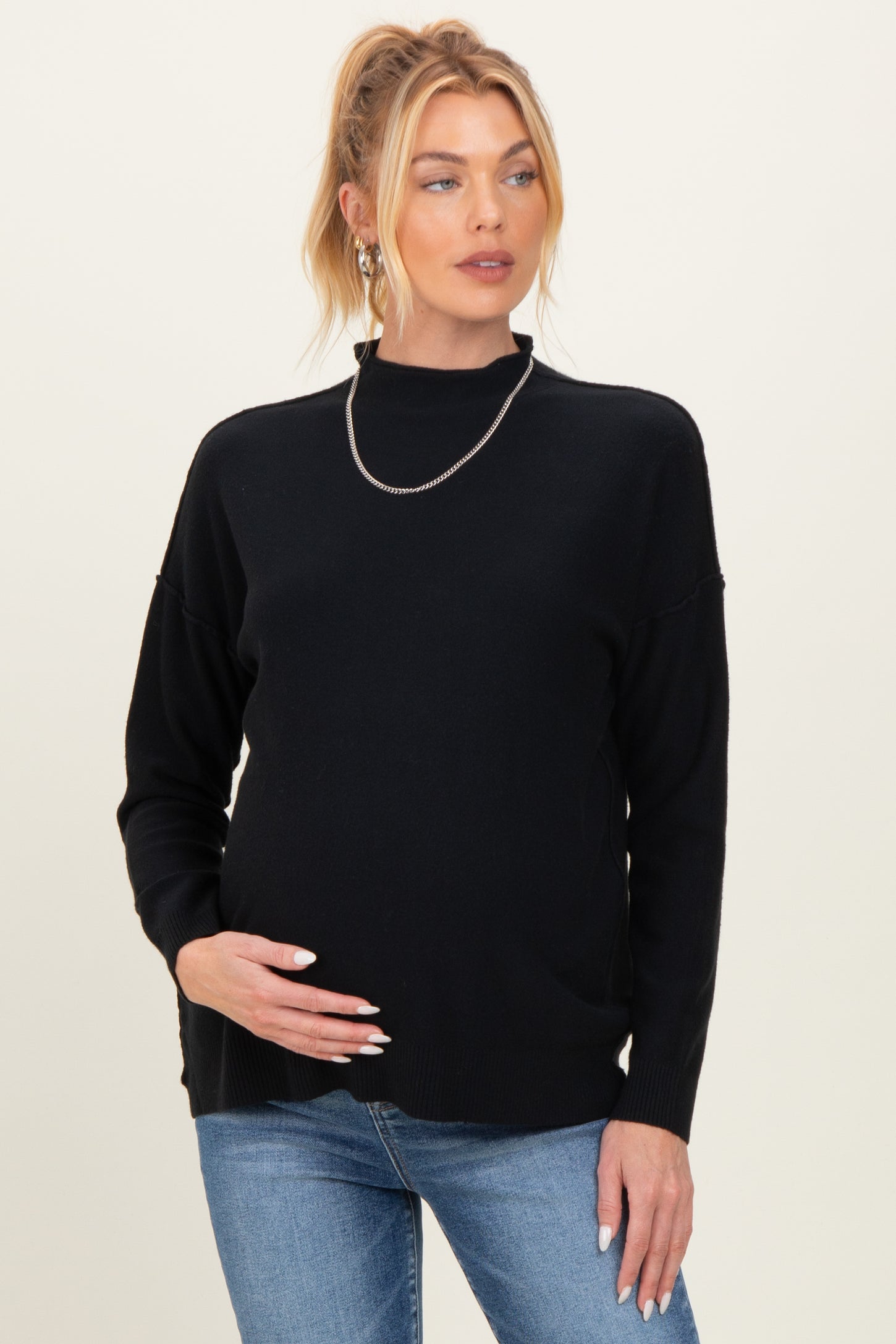 woman wearing a black maternity sweater with a relaxed fit and holding her baby bump