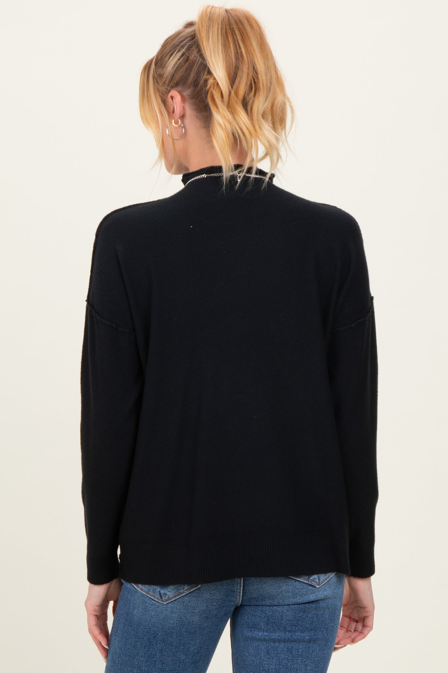 woman wearing a black maternity sweater with a relaxed fit and rolled sleeves, showing the back view