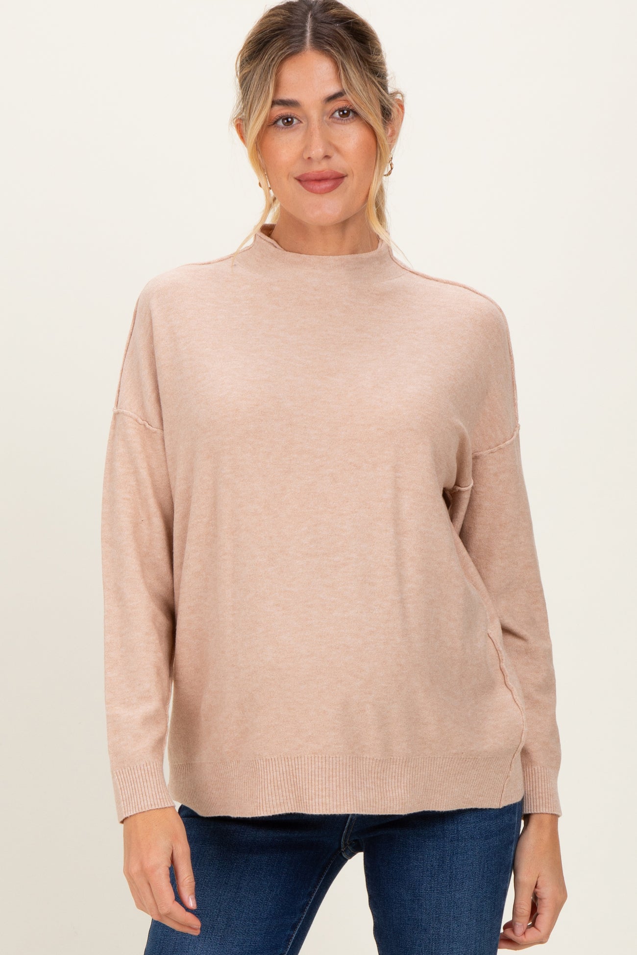 woman wearing a light beige maternity sweater with a relaxed fit and a high neckline