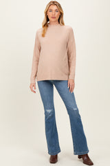 woman wearing a blush pink maternity sweater with a high neckline and distressed flared jeans, showing her baby bump