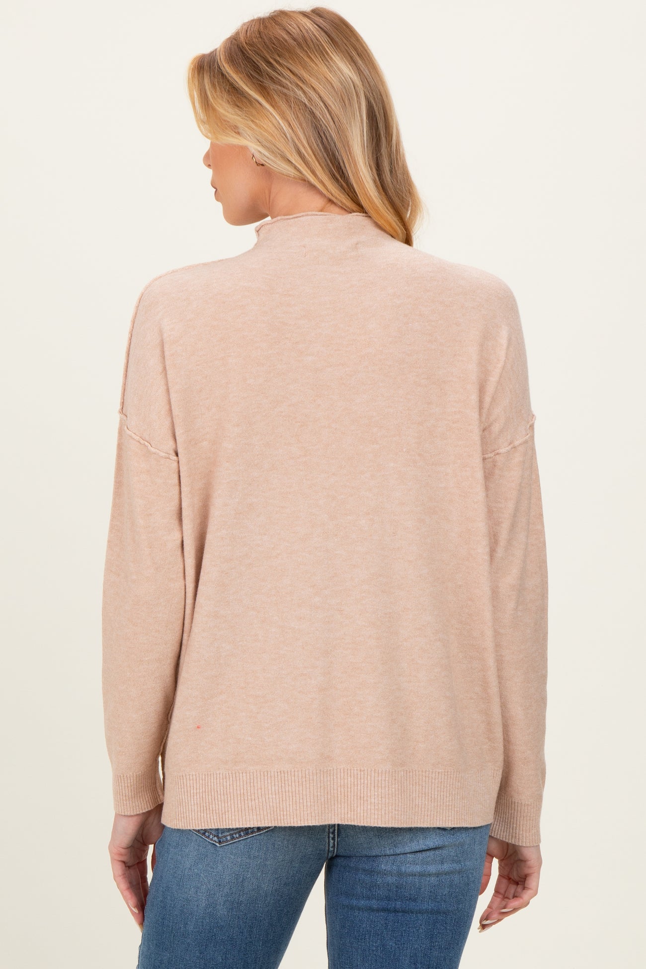 woman wearing a light pink maternity sweater with a relaxed fit and slightly open back, styled with blue jeans