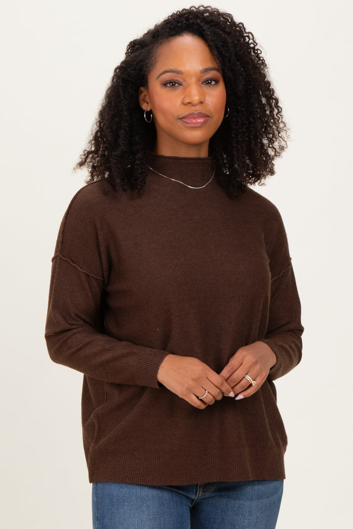 woman wearing a dark brown long sleeve sweater with a high neckline and relaxed fit, styled with light blue jeans