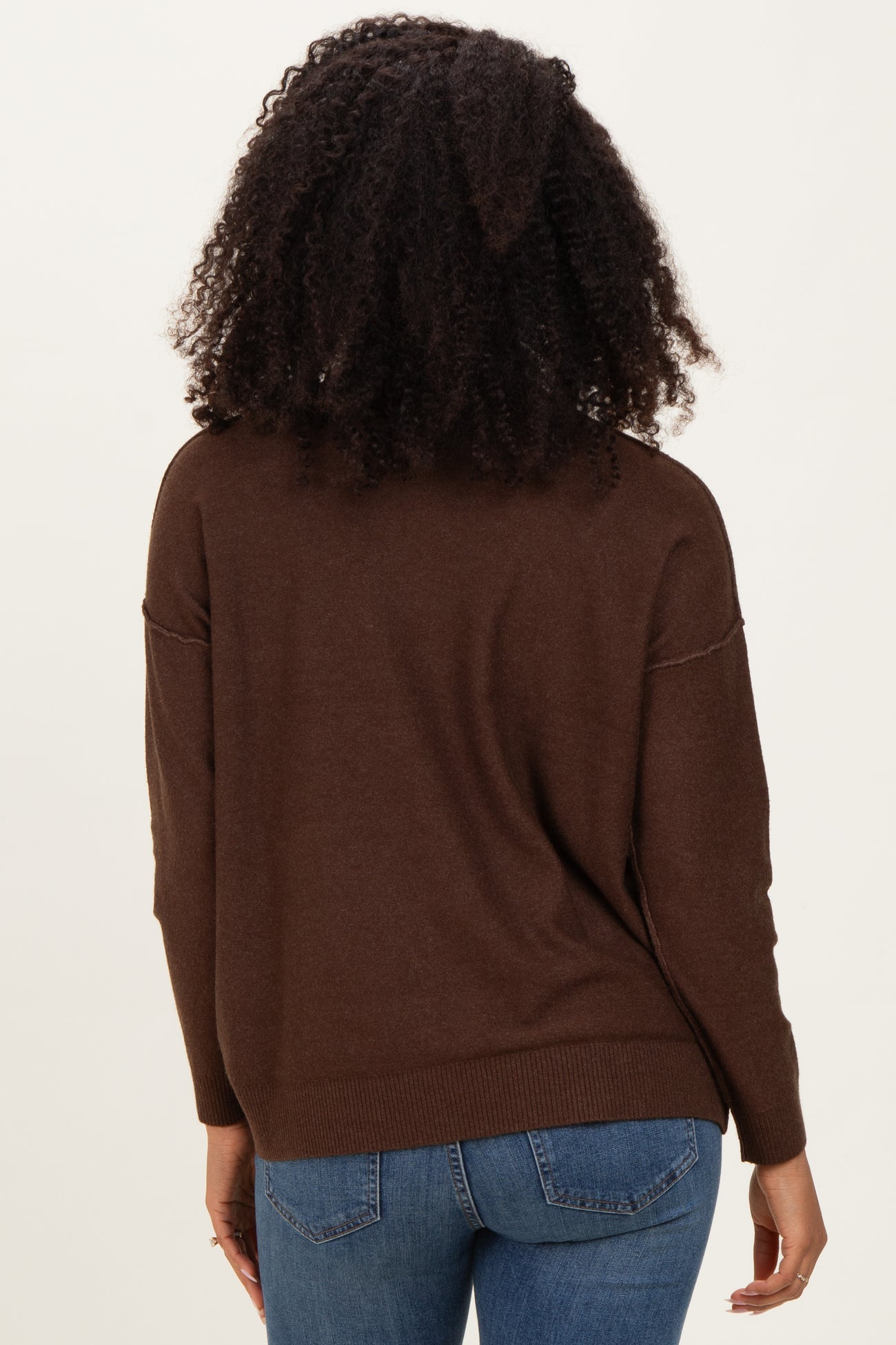 woman wearing a brown oversized sweater with long sleeves and back view, paired with blue jeans
