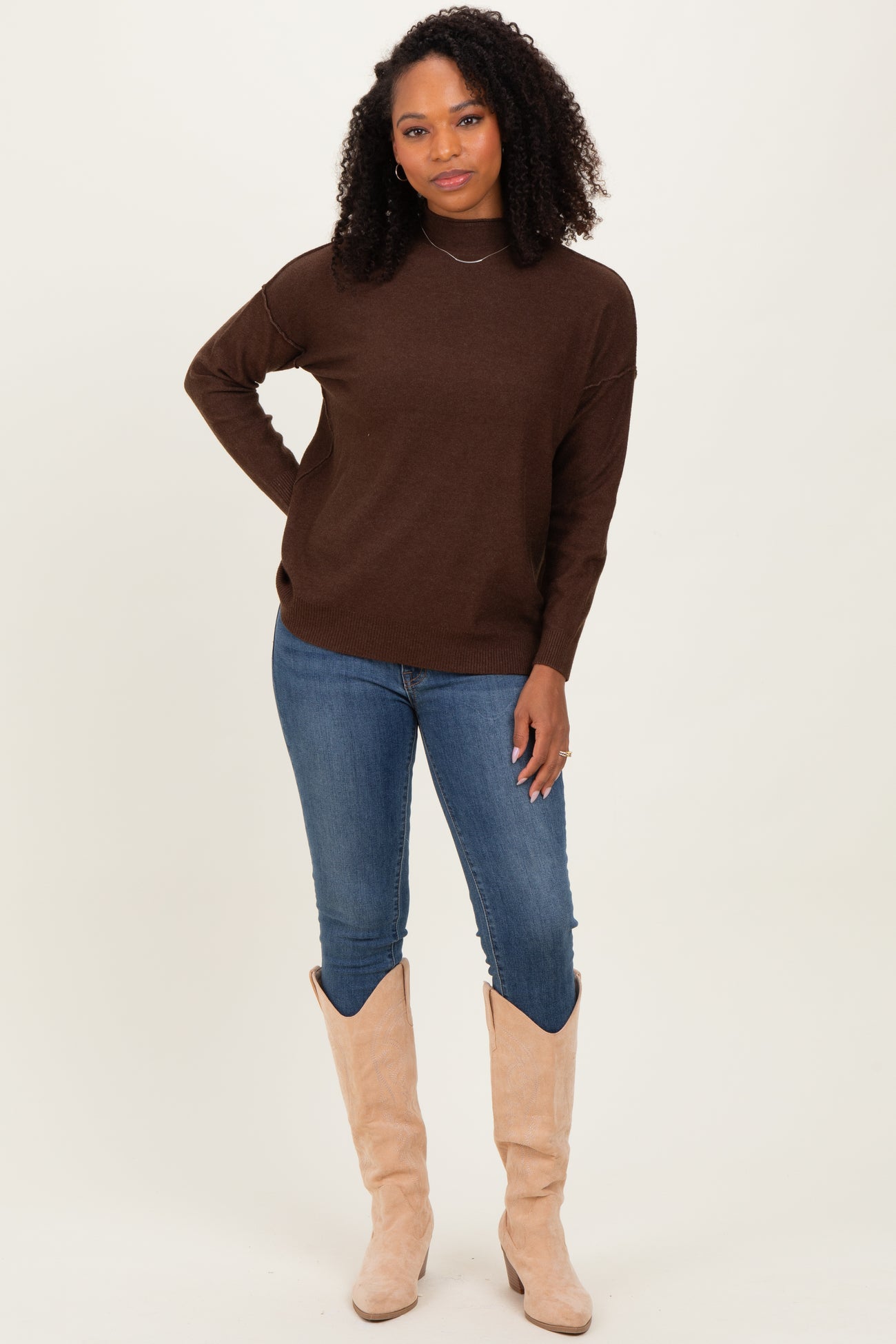 woman wearing a brown knit sweater with a relaxed fit and blue skinny jeans, paired with tall beige boots