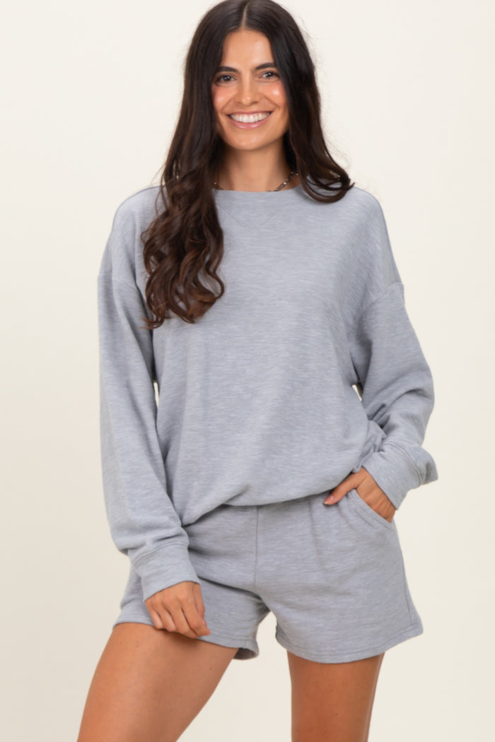 woman wearing a grey long sleeve sweatshirt and matching shorts, smiling at the camera