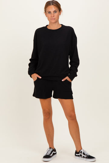 woman wearing a black oversized sweatshirt and matching black shorts, standing with hands in pockets