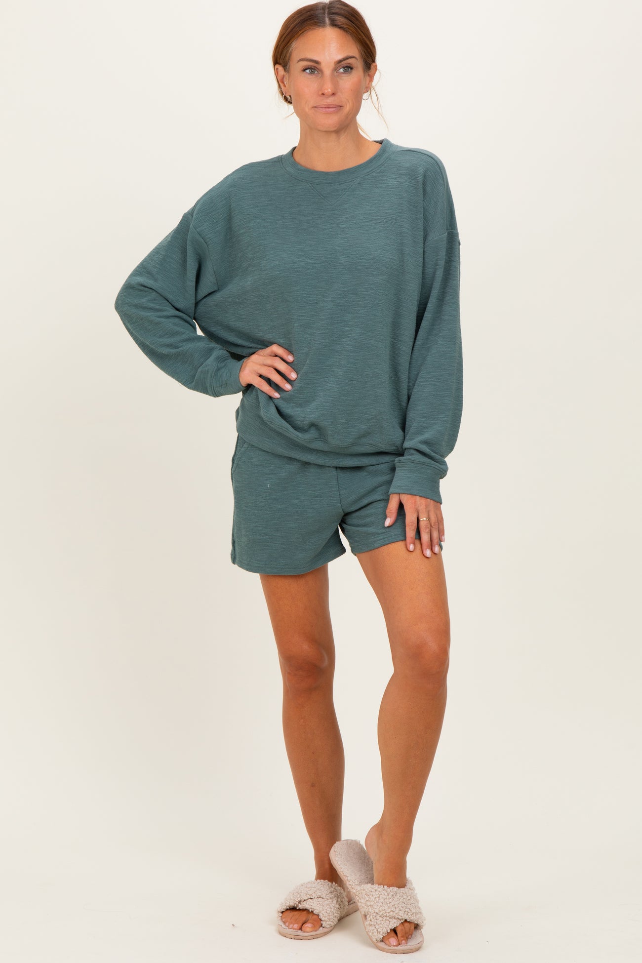 woman wearing a teal oversized sweatshirt and matching shorts, paired with cozy slippers
