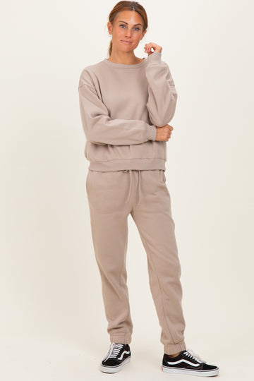woman wearing a beige oversized sweatshirt and matching joggers, styled with black sneakers