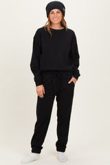 woman wearing a black sweatshirt and black jogger pants, styled with a beanie and cozy socks, standing casually