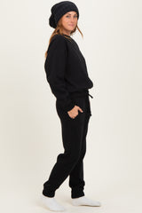 woman wearing a black oversized sweatshirt and matching joggers with a knit beanie and white socks