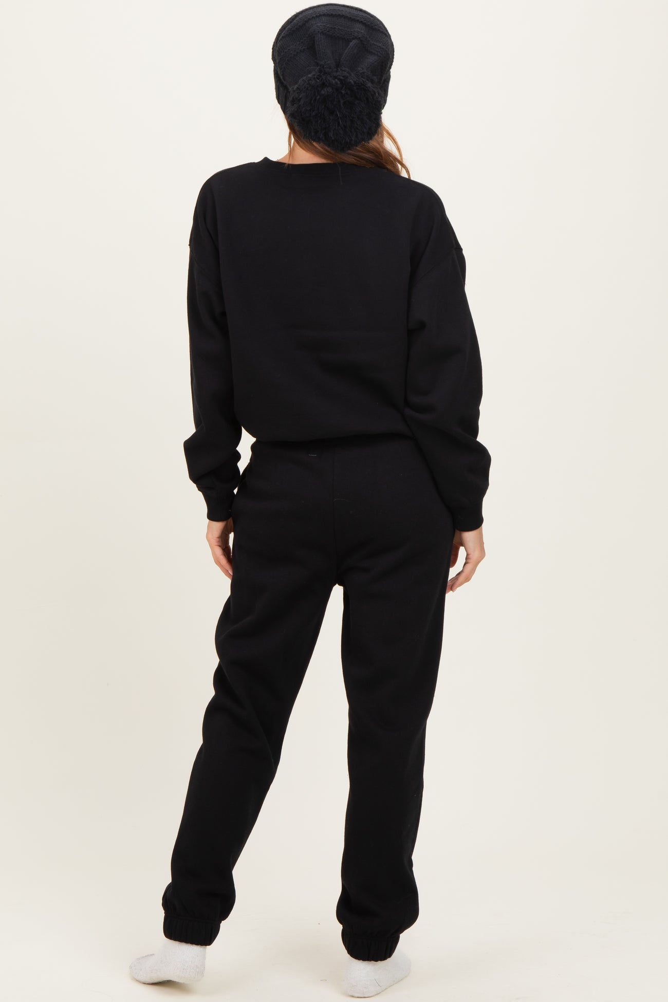 woman wearing a black oversized sweatshirt and matching sweatpants, standing with her back to the camera