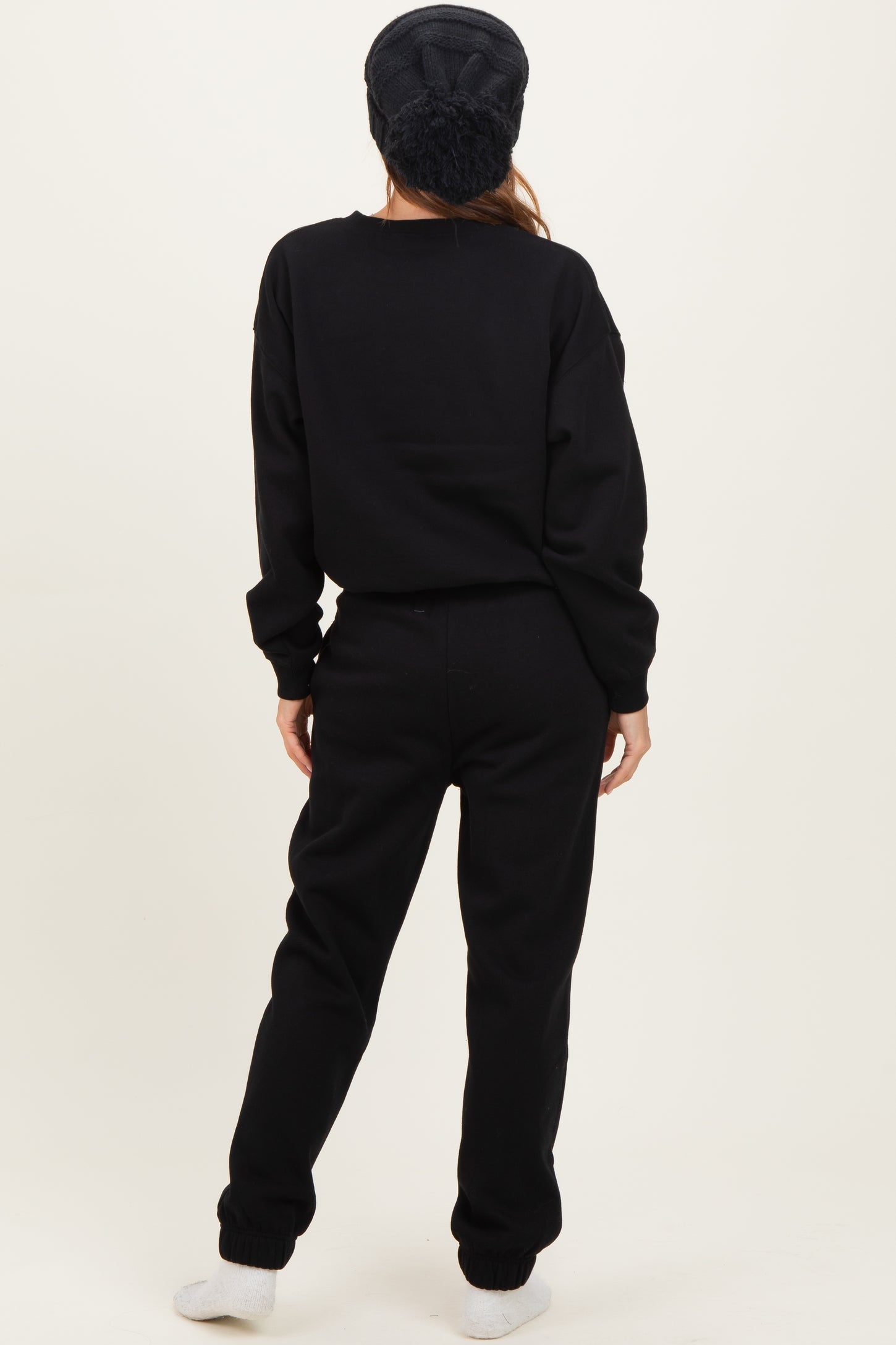 woman wearing a black oversized sweatshirt and matching sweatpants, standing with her back to the camera