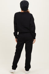 woman wearing a black oversized sweatshirt and matching sweatpants, standing with her back to the camera