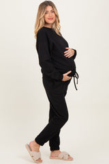 woman wearing a black maternity sweat outfit, holding her baby bump, with fluffy slippers on her feet