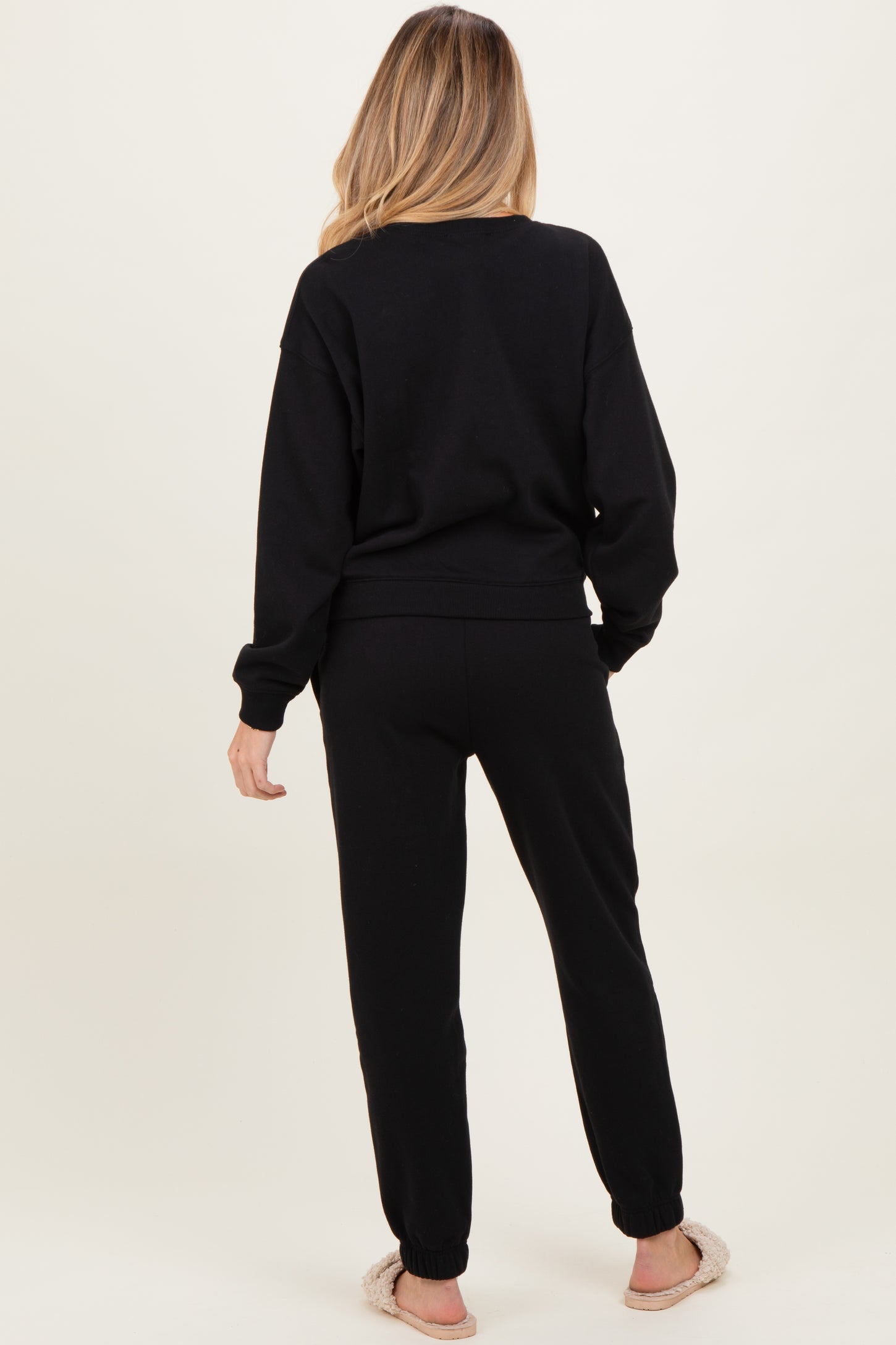 woman wearing a black maternity sweatshirt and matching joggers, with a visible baby bump, viewed from the back