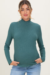 woman wearing a teal ribbed maternity top with a ruffled neckline and holding her baby bump