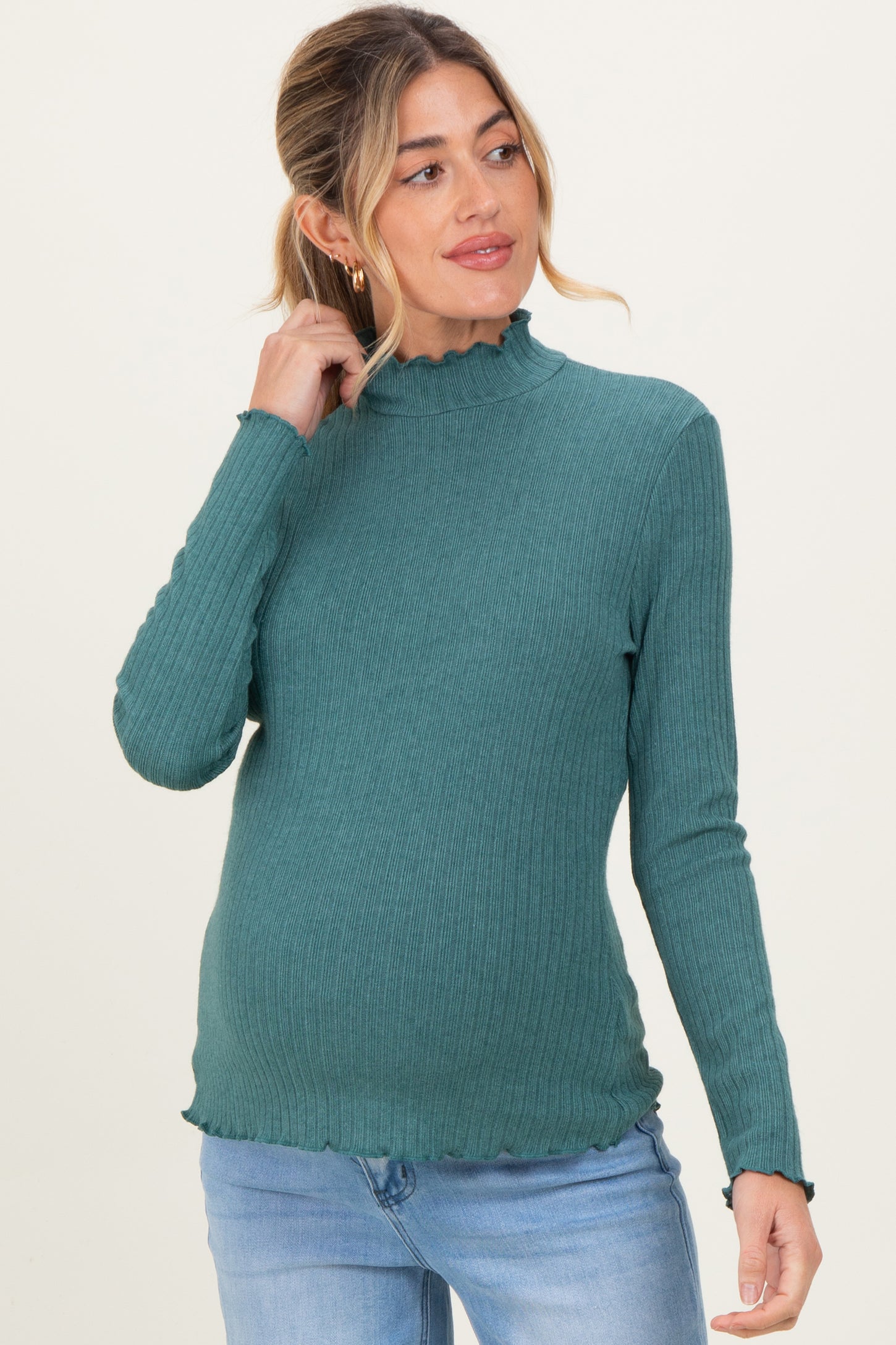 woman wearing a teal ribbed maternity top with ruffle trim and holding her baby bump