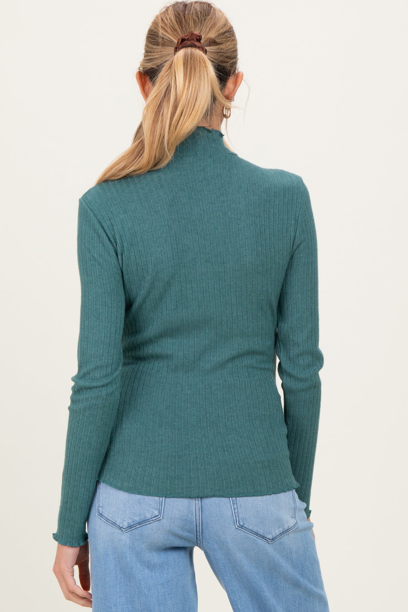 woman wearing a green ribbed long sleeve maternity top seen from the back with casual blue jeans