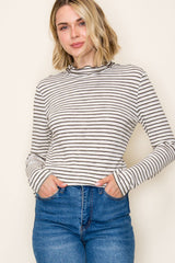 woman wearing a cream and black striped long sleeve top with a mock neck and slim fit, paired with high-waisted blue jeans