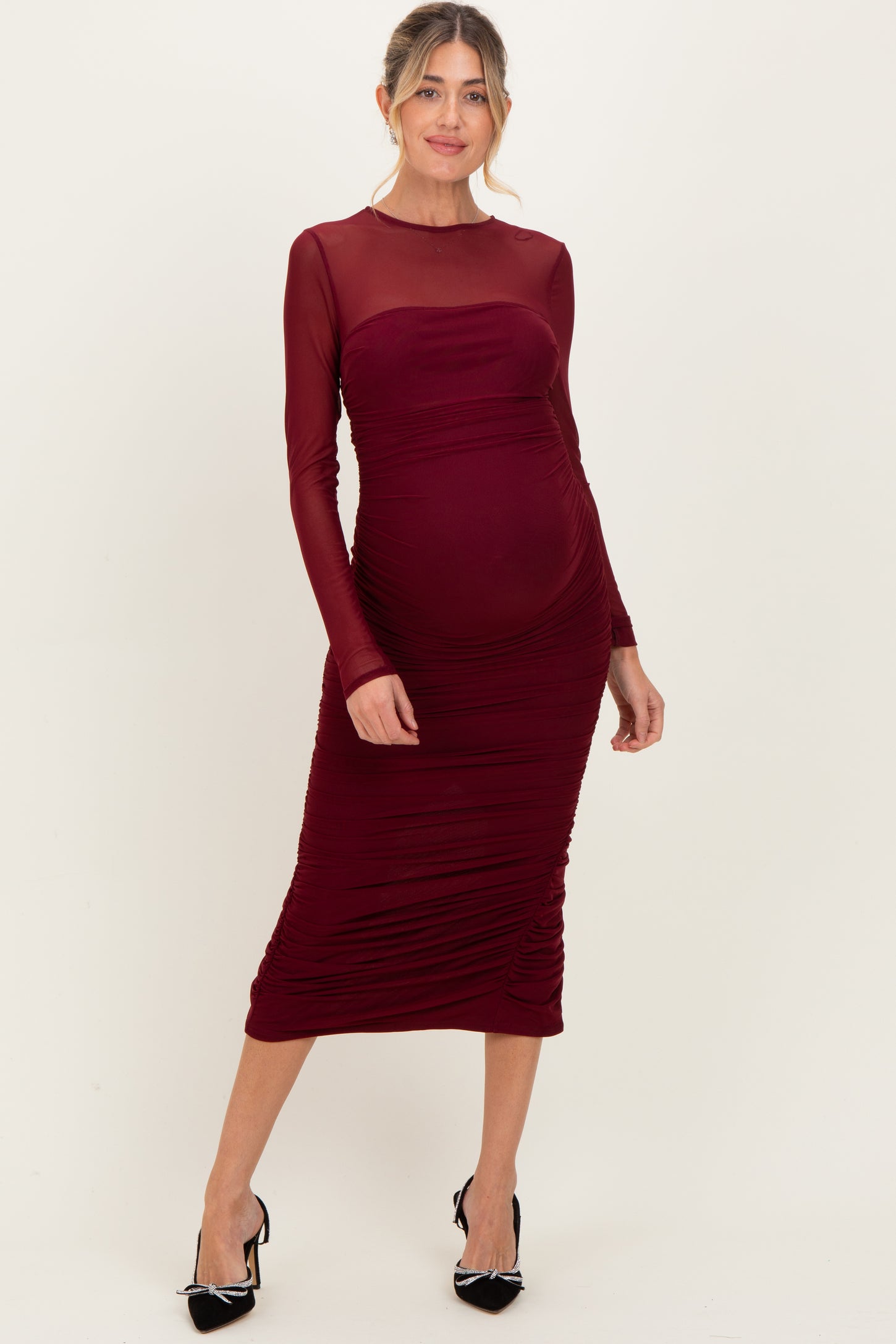 woman wearing a burgundy long sleeve maternity dress with ruched details and a visible baby bump