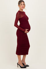 woman wearing a burgundy maternity dress with long sleeves and ruching, highlighting her baby bump