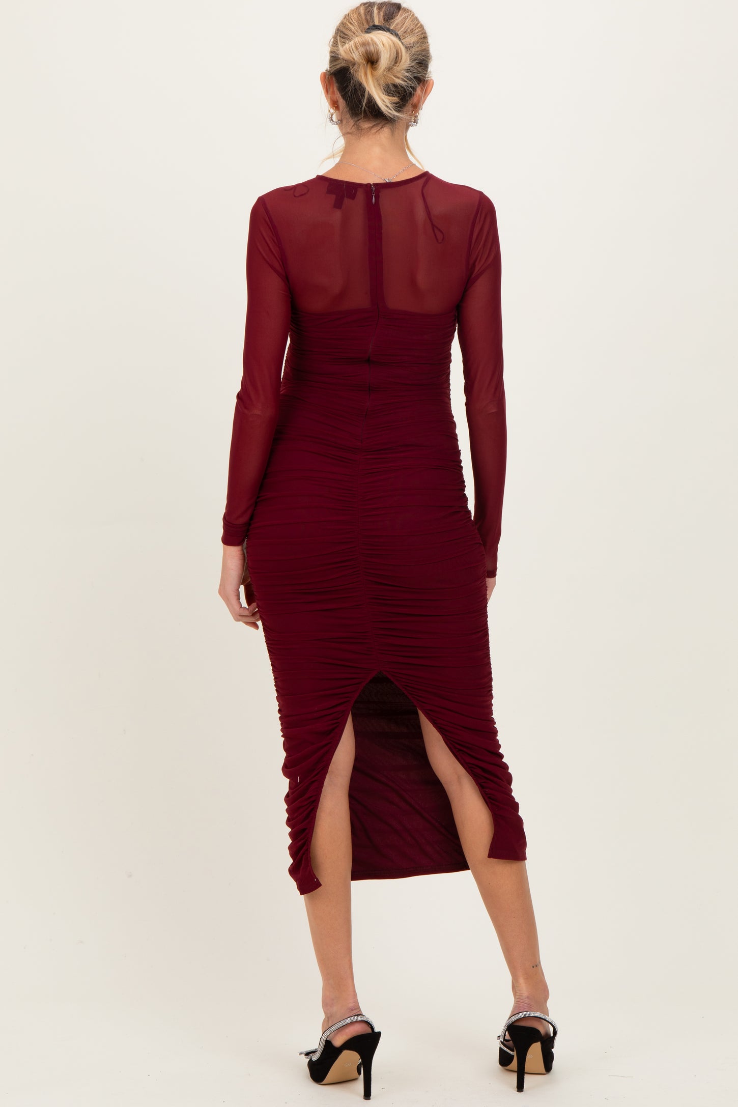 woman wearing a burgundy maternity dress with long sleeves, ruching details, and side slits, showing a baby bump