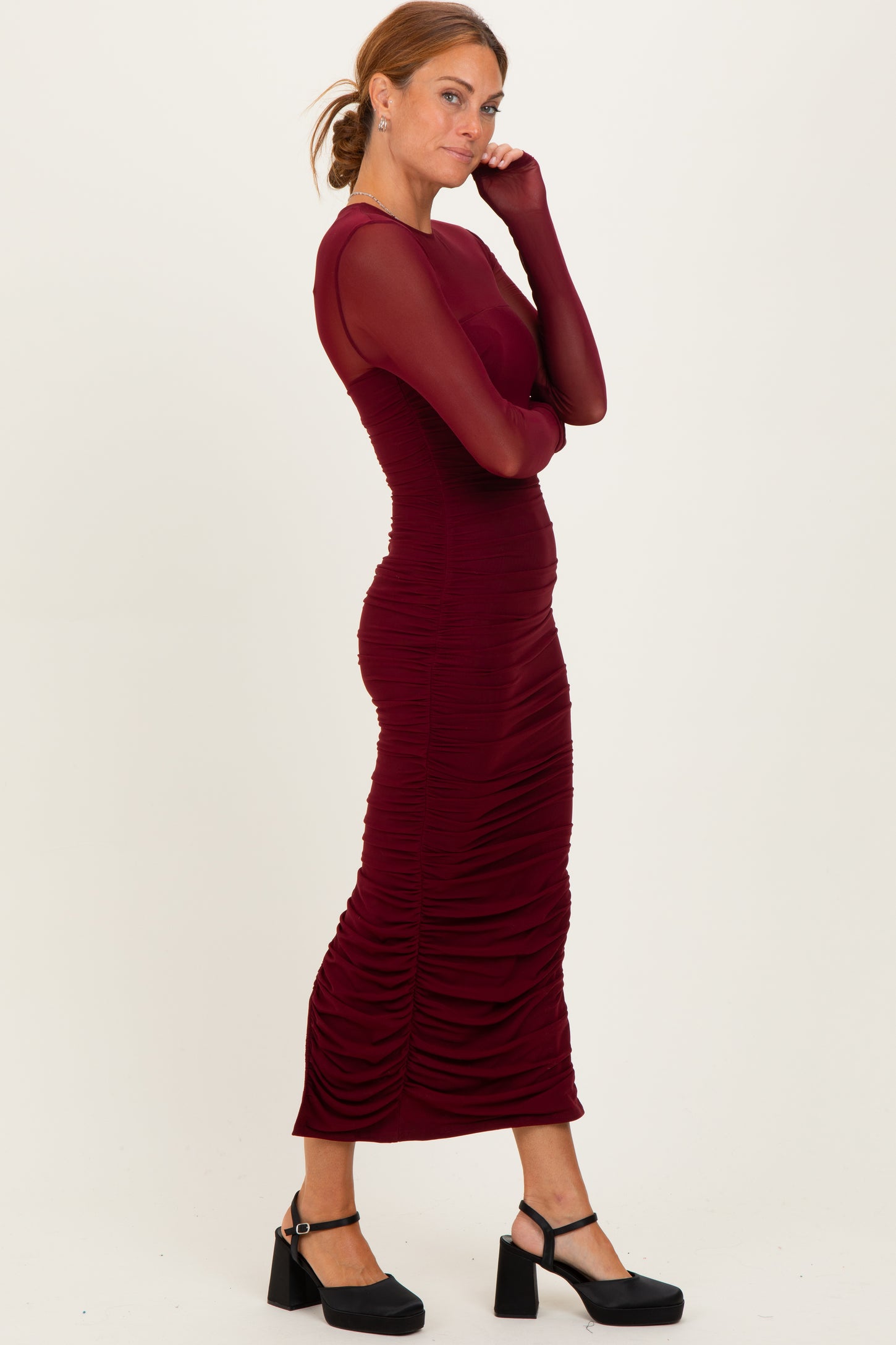 woman wearing a burgundy long sleeve fitted dress with ruching details and a bodycon silhouette