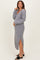 woman wearing a grey maternity sweater dress with a v-neck and side slits, holding her baby bump