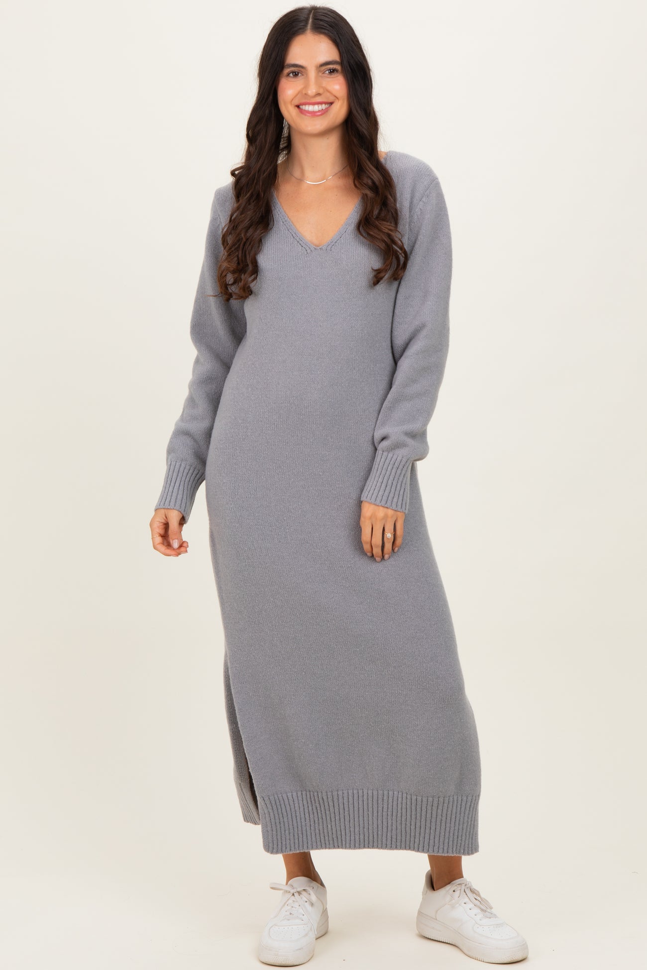 woman wearing a gray long sleeve knit maxi dress with a V-neck and side slits, styled with white sneakers