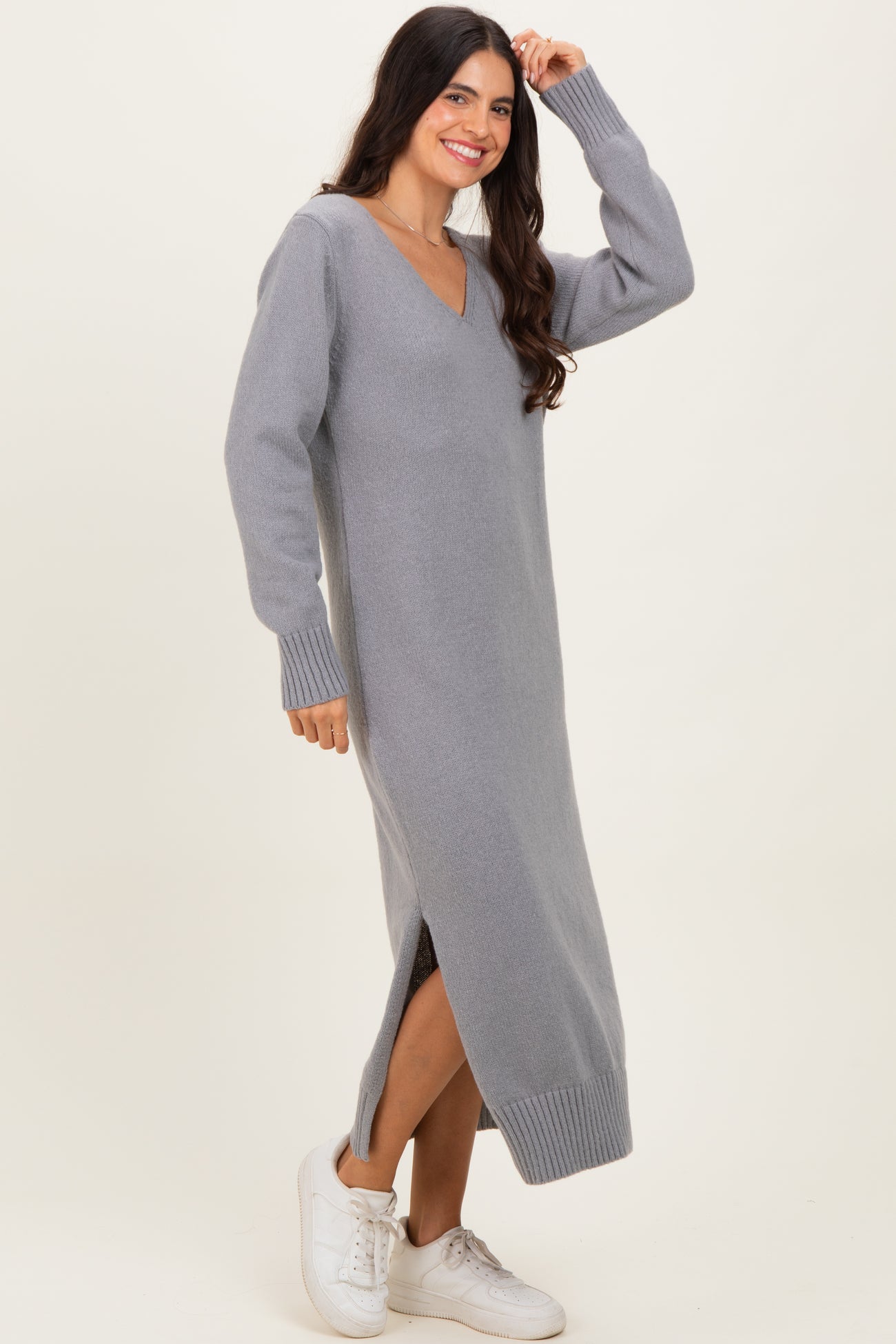 woman wearing a gray long sleeve sweater dress with a v-neck and side slits, paired with white sneakers