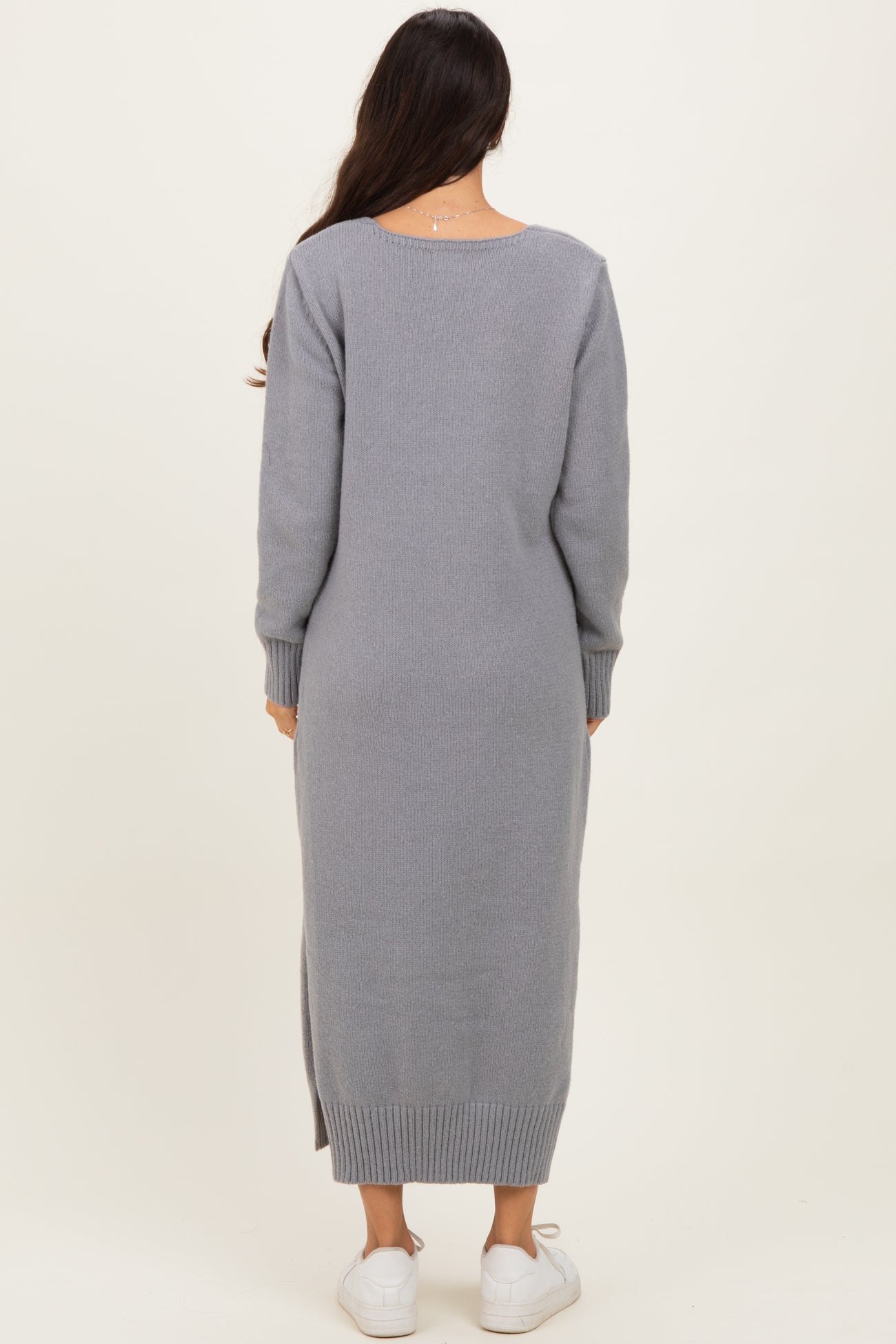 woman wearing a gray long sleeve knit sweater dress with a side slit and white sneakers, viewed from the back