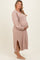 woman wearing a light pink long sleeve maternity dress with side slits and holding her baby bump