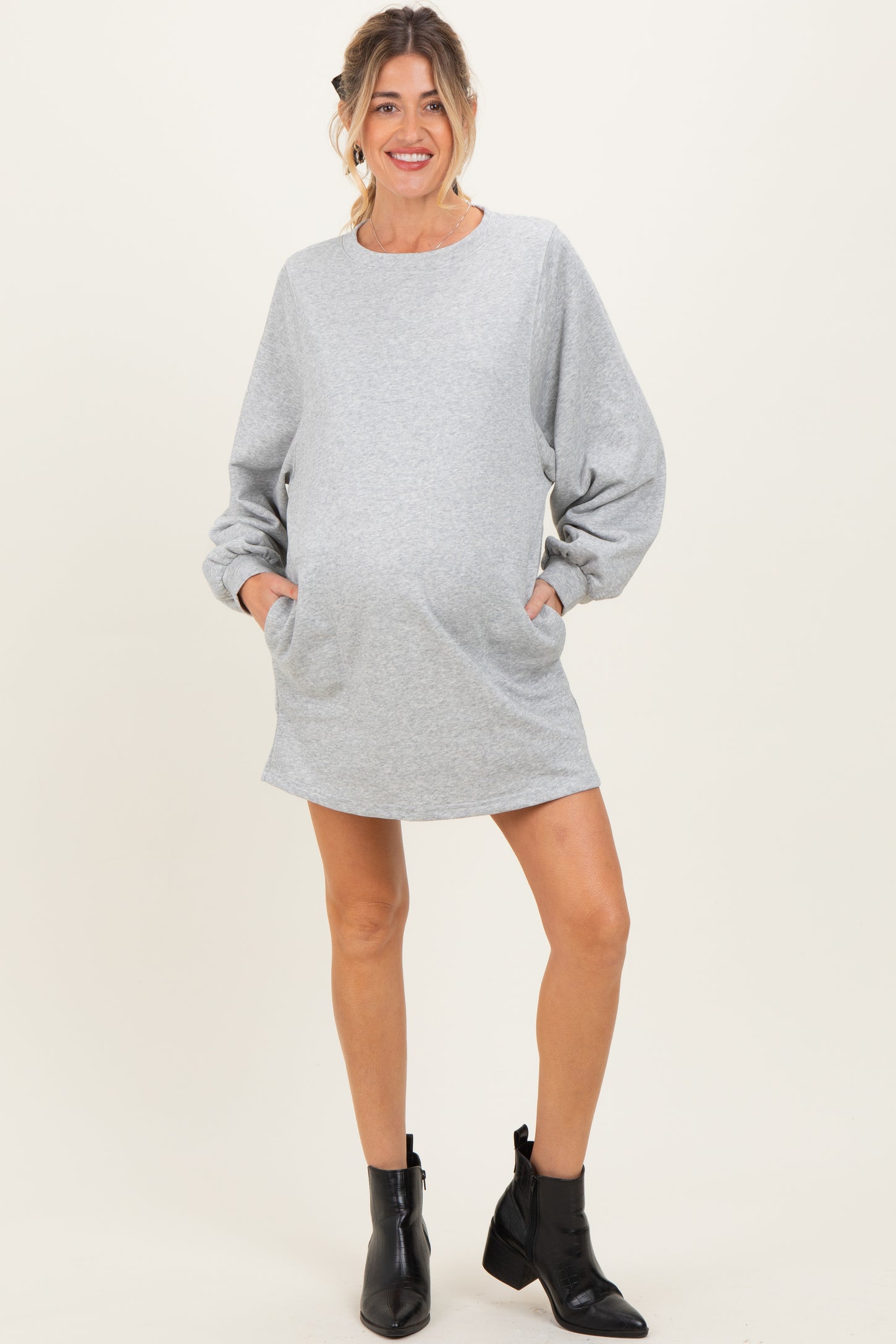 woman wearing a gray maternity sweatshirt dress with balloon sleeves and pockets, showing off her baby bump
