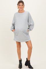 woman wearing a gray maternity sweatshirt dress with balloon sleeves and pockets, showing off her baby bump